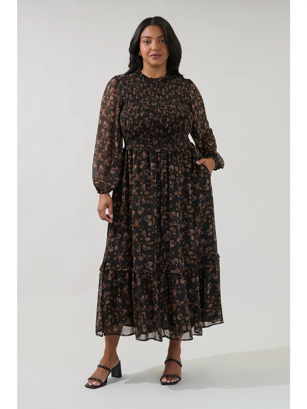 Model wearing a black floral long-sleeve midi dress with a gathered waist and tiered skirt