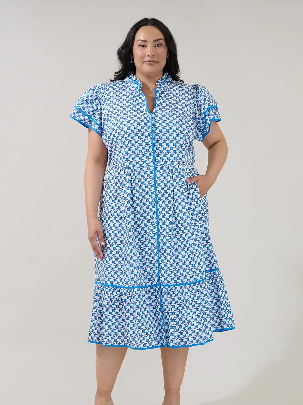 Model wearing a blue and white geometric print tiered midi shirt dress with contrast blue trim and flutter sleeves