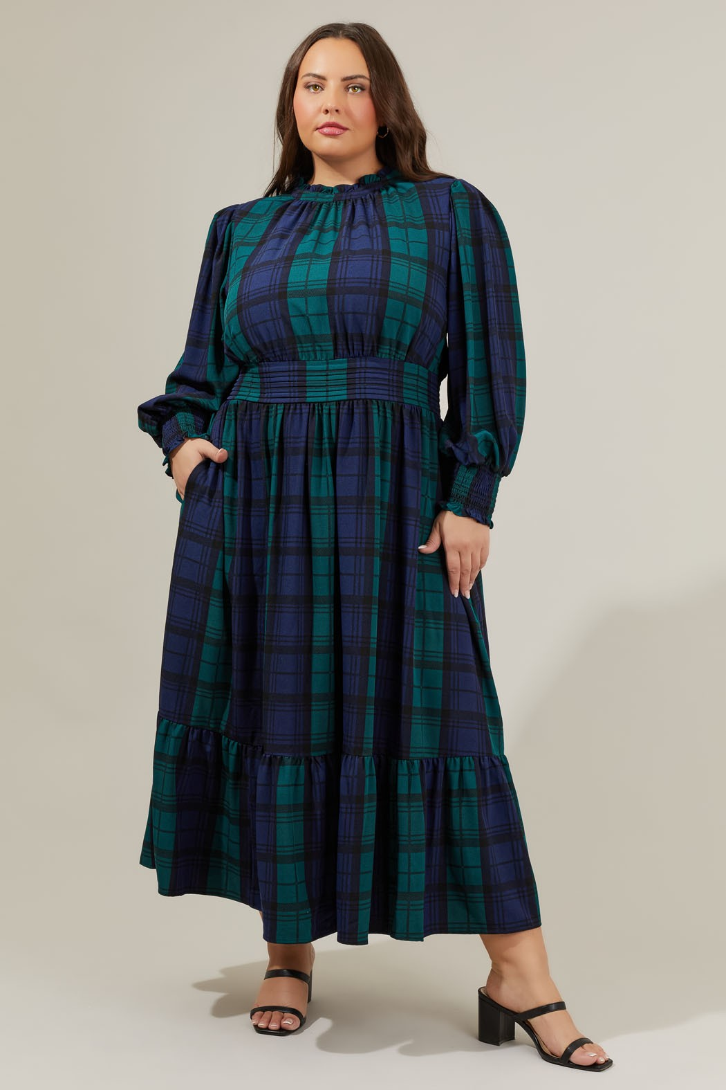Model wearing a green and navy plaid midi dress with long billowy sleeves, a wide cinched waist, and a tiered skirt, styled with black heeled sandals
