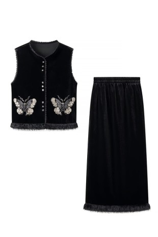 Black sleeveless button-front vest with two large embellished butterfly appliqués, styled with a long black skirt with a fringe-trimmed hem.