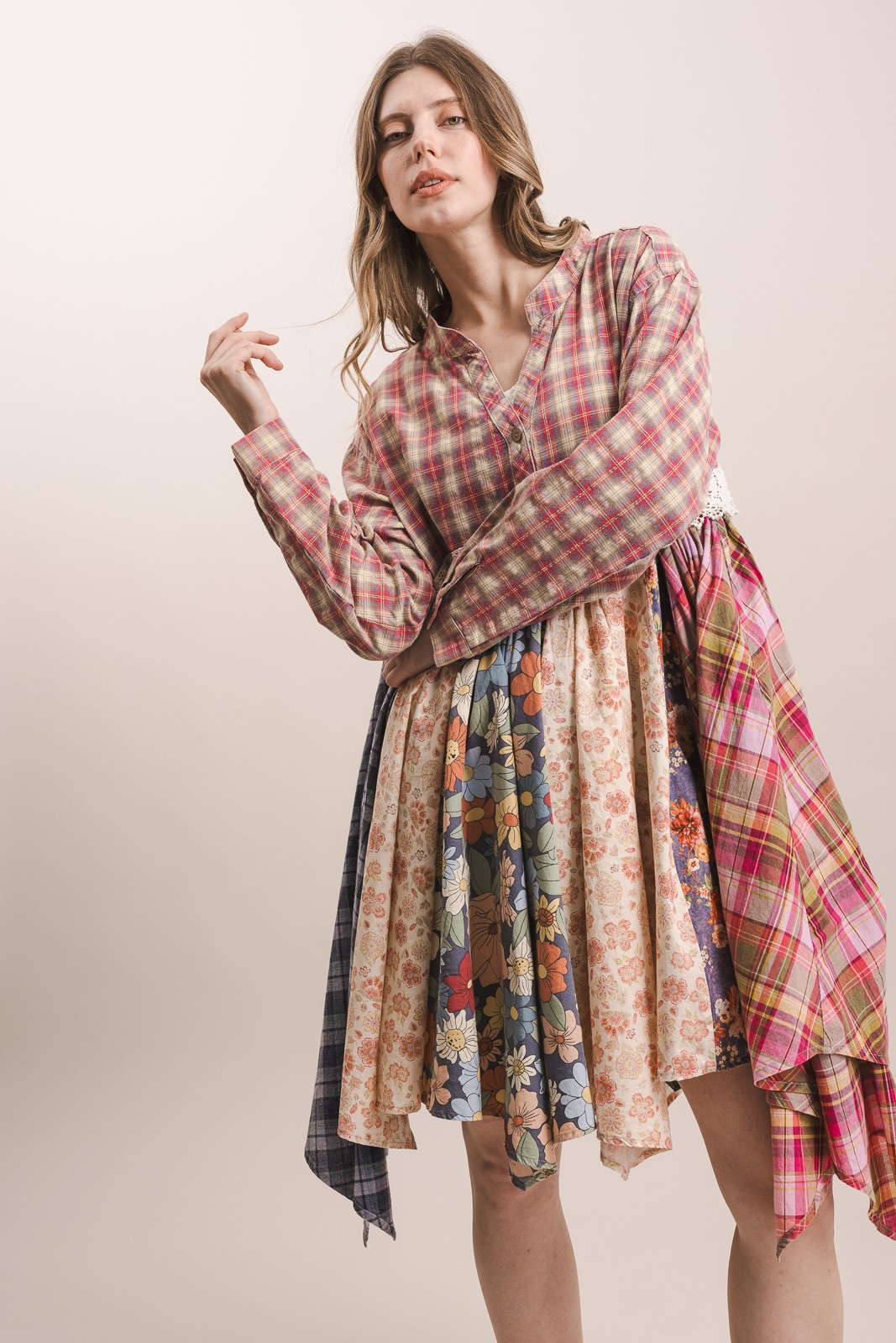 Model wearing a long-sleeve pink and taupe plaid dress with floral patchwork panels and an asymmetric handkerchief hem.