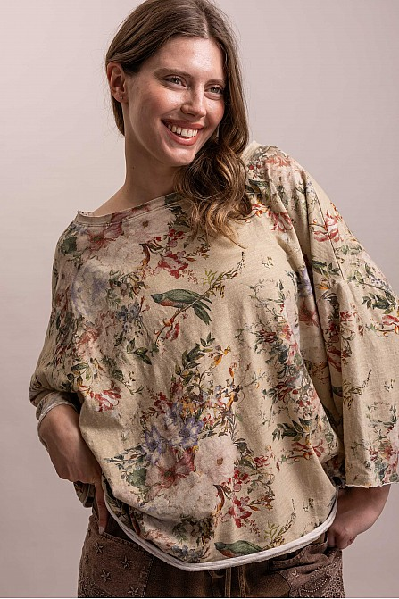 Model wearing a beige floral dolman top with muted pink and lavender flowers, green leaves, and a wide round neckline.