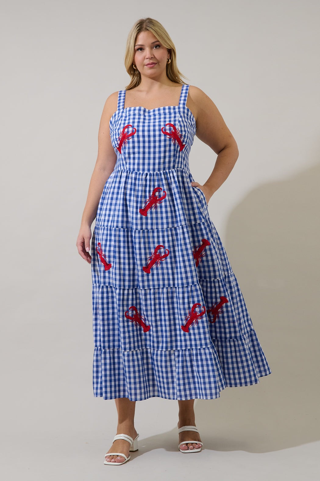 Model wearing a blue gingham tiered maxi dress with red embroidered lobsters and white sandals