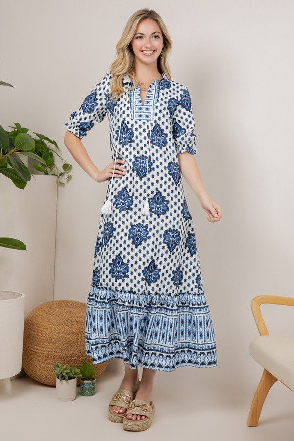 Model wearing a blue-and-white floral maxi dress with a tassel-tie neckline, three-quarter sleeves, and border-print hem