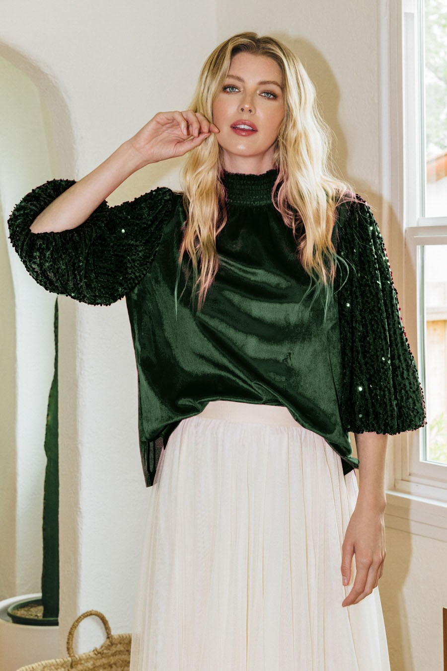 Model wearing dark mock-neck blouse with sparkling sequin sleeves and light skirt