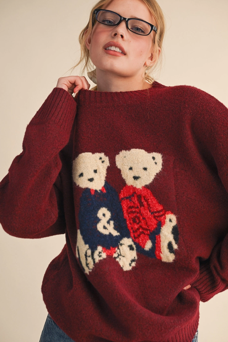 Burgundy crewneck knit sweater with two cream teddy bears dressed in navy and red.