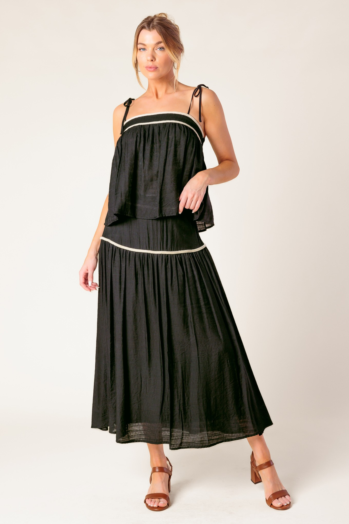 Model wearing a black sleeveless top with white piping and a matching long skirt