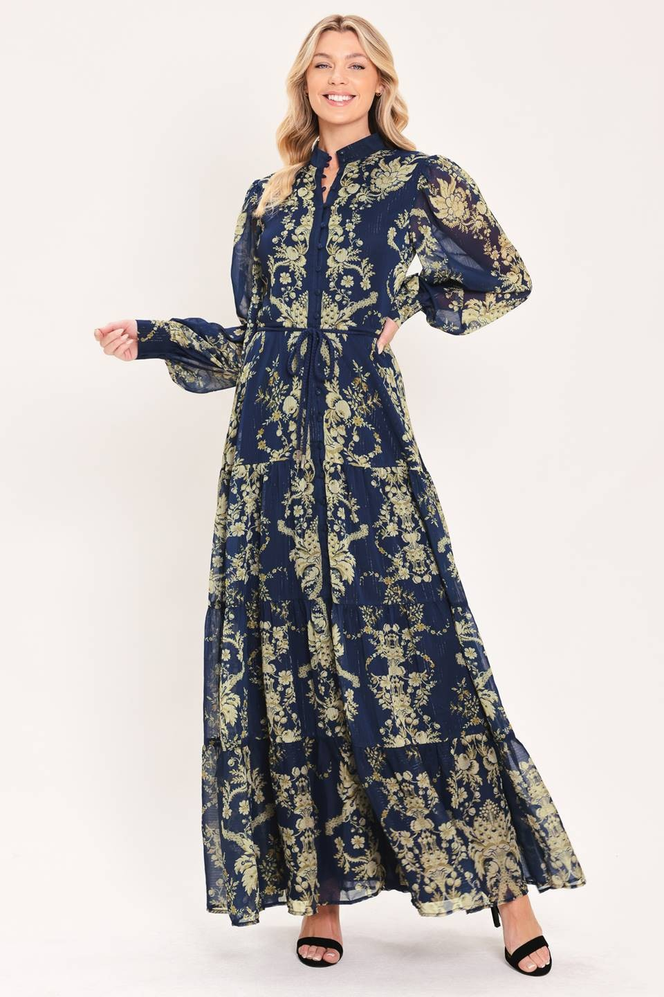 Model wearing a navy floral maxi dress with long sleeves, a tie waist, and a flowing tiered skirt