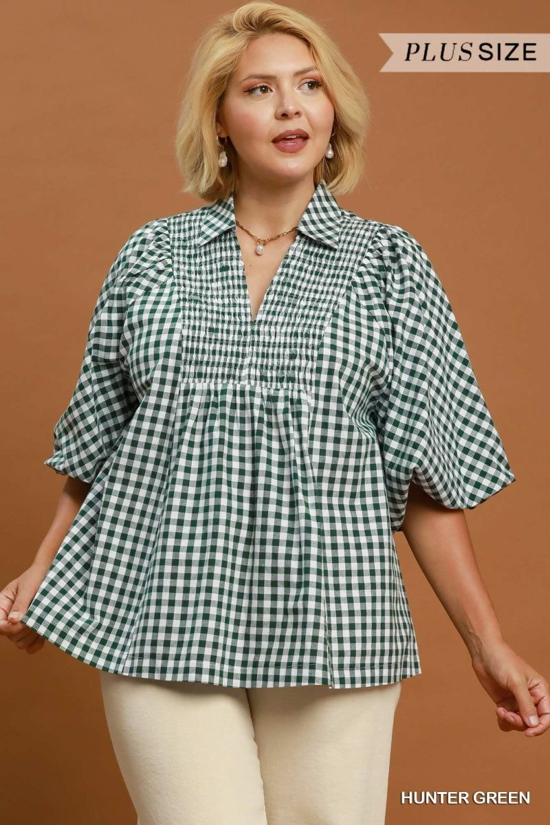 Plus size model wearing a hunter green gingham blouse with puff sleeves, split notch collar, and shirred yoke, paired with light-colored pants
