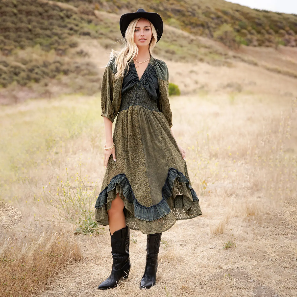 Model wearing an olive patterned midi dress with a black gathered V-neck bodice, voluminous sleeves, and black ruffle hem