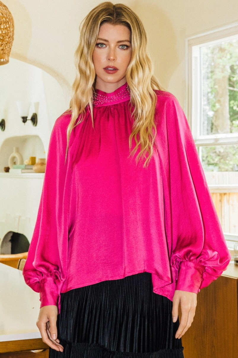 Model wearing a hot pink satin blouse with balloon sleeves and a sparkling embellished mock neck