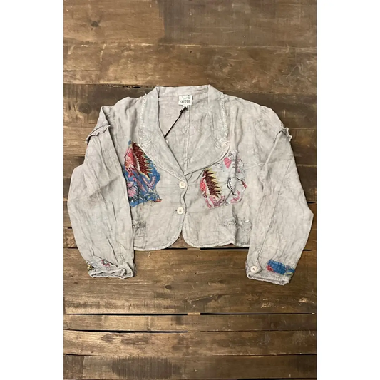Front of gray-taupe cropped jacket with colorful patterned patches, two buttons, and long sleeves.