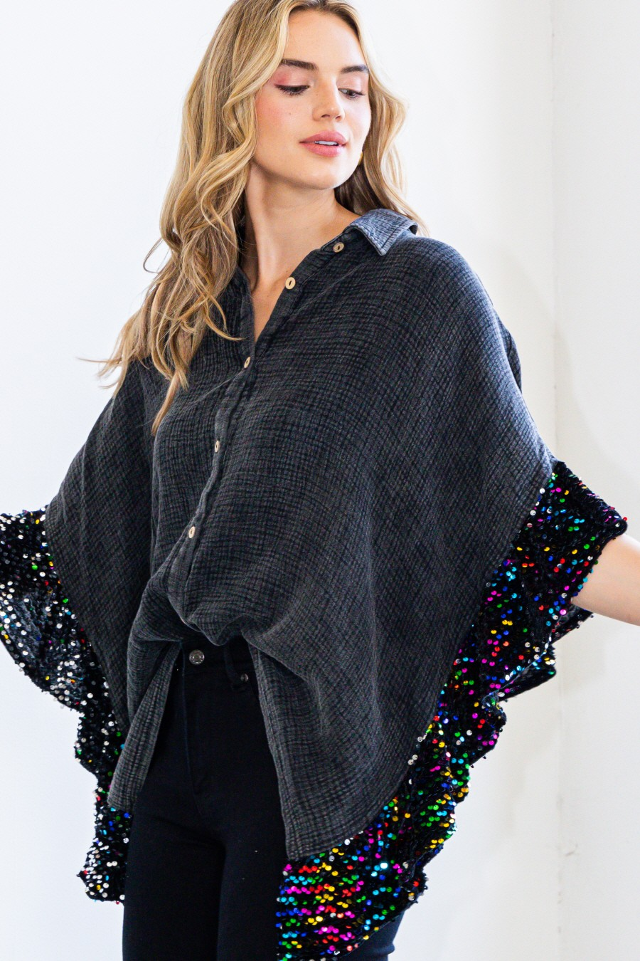 Woman wearing an oversized charcoal textured button-up top with cascading rainbow multicolor sequin ruffle trim