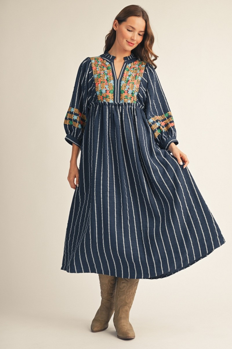 Model wearing a navy striped midi dress with colorful floral detailing, three-quarter sleeves, and tan boots.