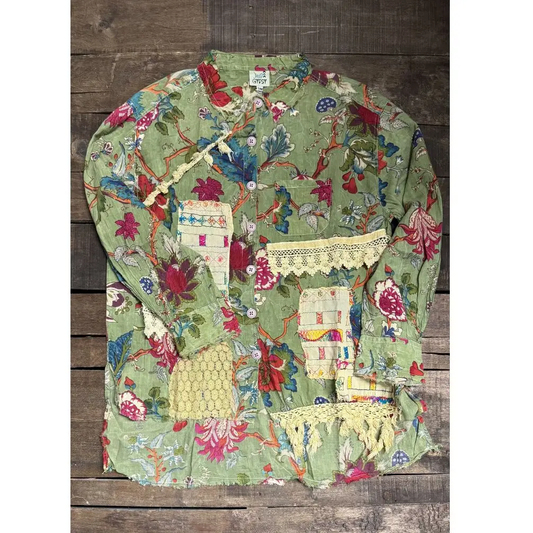 Sage green floral button-up blouse laid flat, with patchwork pockets, cream crochet lace trim, decorative fabric patches, long sleeves, and a band collar