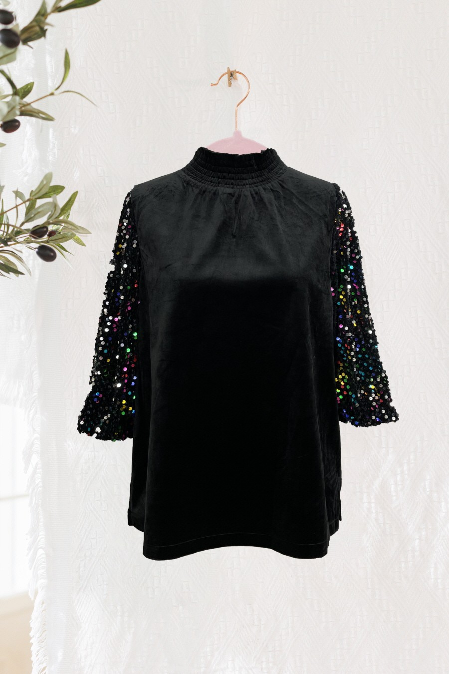 Black mock-neck blouse with sparkling sequin sleeves on a hanger