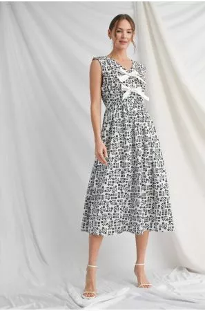Model wearing a black-and-white printed sleeveless midi dress with three white front bows and a flared skirt.